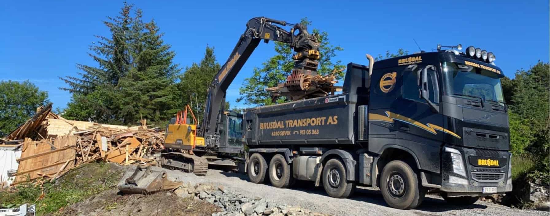 En stor lastebil fra Brusdal Transport AS blir lastet med rivningsmateriale ved en byggeplass.